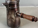 an old silver coffee pot with a wooden handle on a table