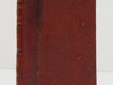 an old book with a red cover sitting on top of a white table