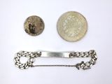 two silver coins and a silver tie bar on a white surface