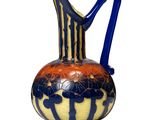 a vase with a blue handle on a white surface