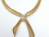 a close up of a gold necklace with a bow on a white background