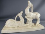statue of a bird and a deer on a rock with a body of water in the foreground