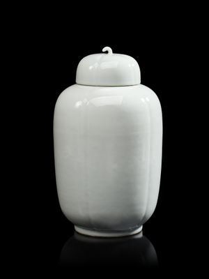 un vase blanc muni d'un couvercle, posé sur une surface noire