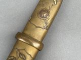 a close up of a gold colored knife with a bird and flower design on it