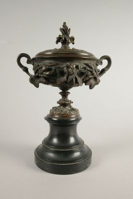 une urne en bronze posée sur un socle noir, sur fond blanc
