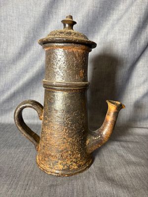 une vieille théière en métal avec une poignée en bois, sur fond gris