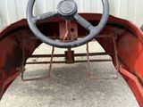 an old red car with a steering wheel is parked in front of a building