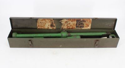 une vieille pipe verte dans un étui en métal posé sur une surface blanche