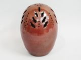 a red vase with holes in it on a white surface