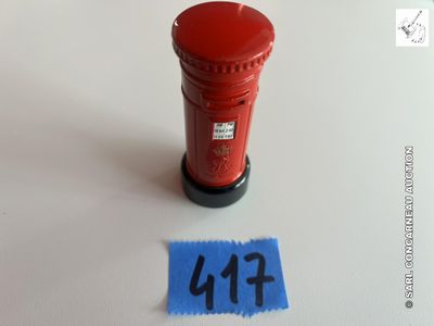 une boîte aux lettres rouge posée sur une surface blanche, à côté d'un morceau de papier bleu