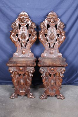 une paire de chaises anciennes en bois sculpté sur des socles, devant un fond bleu