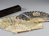 Plusieurs éventails chinois anciens sont posés sur une table, à côté d'une boîte