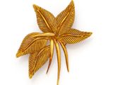 a close up of a gold leaf brooch on a white background