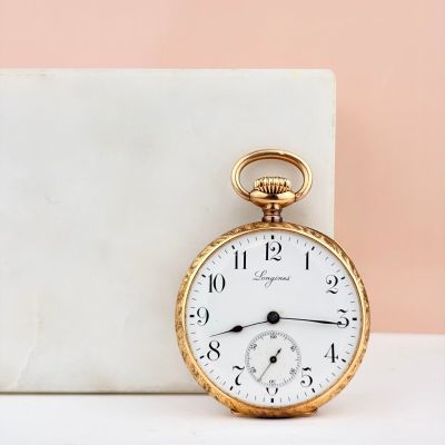 une montre de poche ancienne posée sur un bloc de marbre, à côté d'un autre bloc de marbre