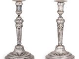 une paire de bougeoirs anciens en argent posés sur des socles, sur fond blanc