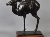 bronze statue of a deer on a wooden base on a gray background