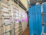 Plusieurs échelles sont alignées dans une pièce dont la porte est bleue