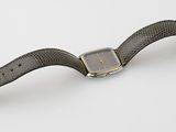 une photo d'une montre posée sur une surface blanche, avec un bracelet noir