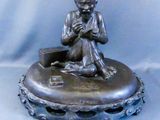 statue d'un garçon assis sur un plateau en argent, tenant un livre