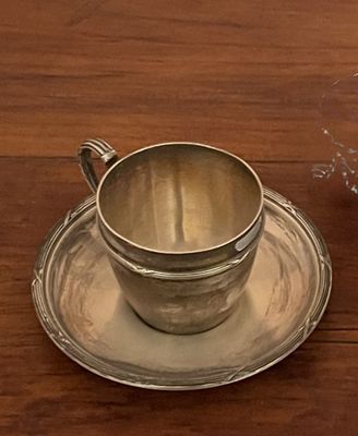 a silver cup and saucer sitting on a wooden table
