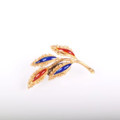 un gros plan sur une broche en or ornée de feuilles rouges, bleues et jaunes