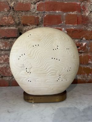un vase blanc posé sur une table, avec un mur de briques en arrière-plan