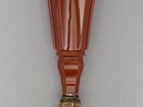 un vase en verre orange avec un socle doré posé sur une surface blanche