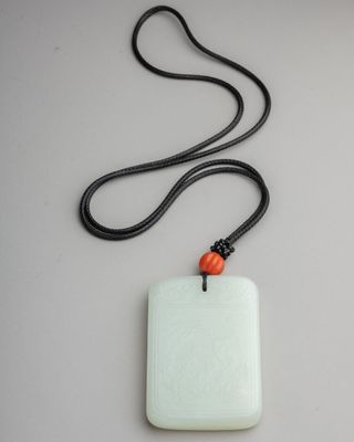 white jade pendant with a red bead on a black cord
