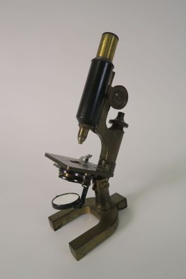 an old microscope is sitting on a stand on a white surface