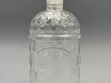une bouteille en verre transparent avec un bouchon argenté, posée sur une surface grise