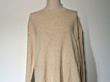un pull à col roulé beige sur un mannequin posé contre un mur blanc