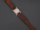 a silver watch with brown leather strap on a gray background