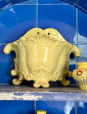 un vase jaune posé sur une étagère, à côté d'un mur carrelé de bleu