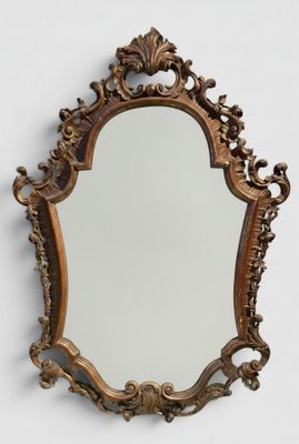 Un miroir richement sculpté est accroché au mur d'une pièce blanche.