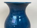 a blue vase sitting on a table with a white wall in the background
