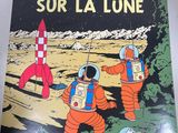 a person holding up a book with an image of astronauts on the moon