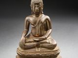 statue en bronze représentant un Bouddha assis sur un socle, sur fond noir