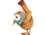 une image représentant une broche en forme d'oiseau en or, ornée de pierres turquoise et rouges