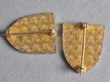 two pieces of gold leaf brooches on a white surface
