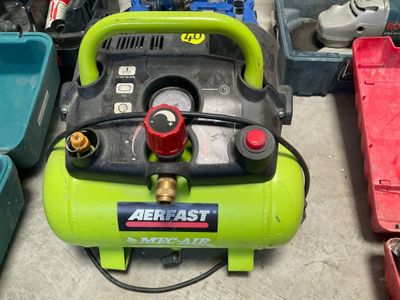 un compresseur d'air vert posé par terre à côté d'autres outils