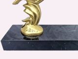 a gold statue of a woman holding a tennis racquet on top of a marble base