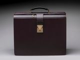porte-documents en cuir marron avec fermoir et poignée en laiton sur fond gris