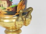 a gold vase with a painting on it sitting on a stand