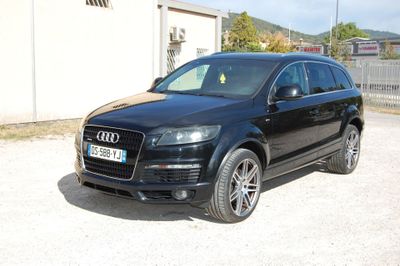 un SUV Audi noir garé devant un immeuble, sur un parking en gravier