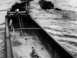Photographie en noir et blanc d'un bateau sur une rivière, avec un pont en arrière-plan