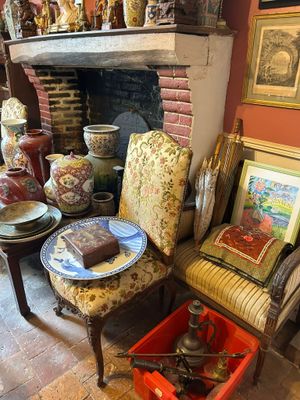 une pièce avec une cheminée, un fauteuil, une table et des tableaux accrochés au mur