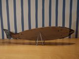 a wooden fish sculpture on a table with a blue striped wall behind it
