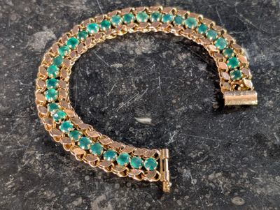 bracelet plaqué or orné de perles de verre vertes sur un fond marbré