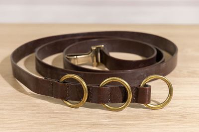 un collier de chien en cuir marron avec des anneaux en laiton posé sur une table en bois