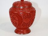 un vase rouge muni d'un couvercle, posé sur une surface blanche